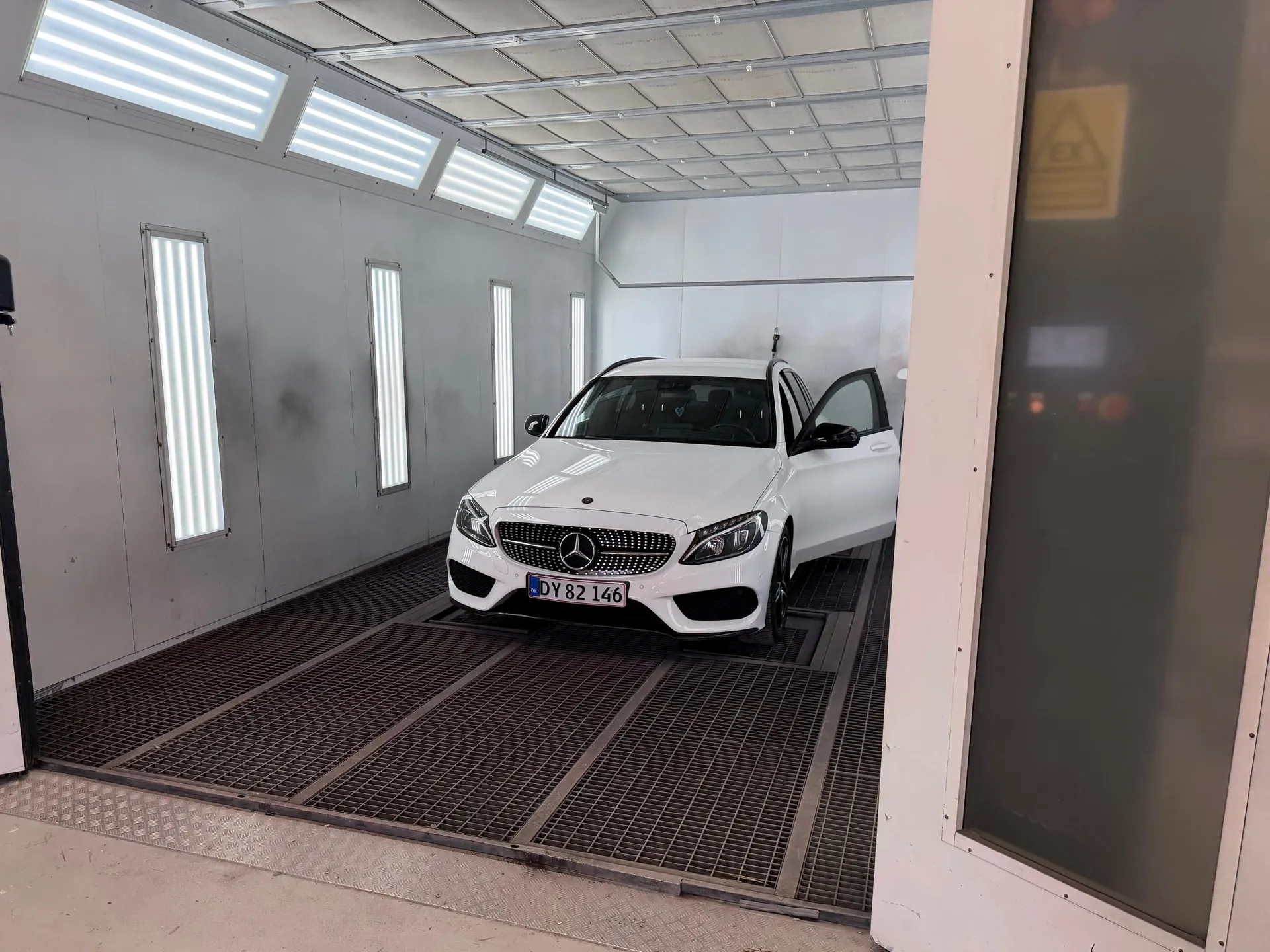 Spray booth with white Mercedes C-class on the lift — premium craft signal