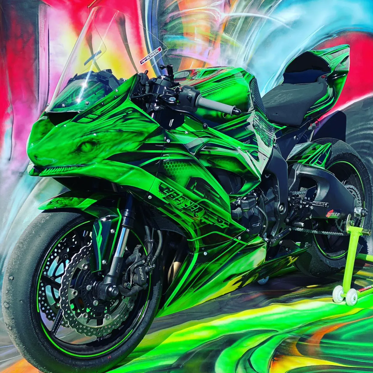 Grøn Kawasaki motorcykel med Sergios håndlagte airbrush-mønster, foran kulisse med samme mønster