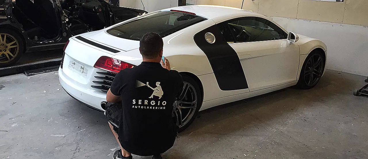 Sergio i en Sergio Autolakering-polo, kigger på en hvid Audi R8 med sorte racerstriber inde i værkstedet